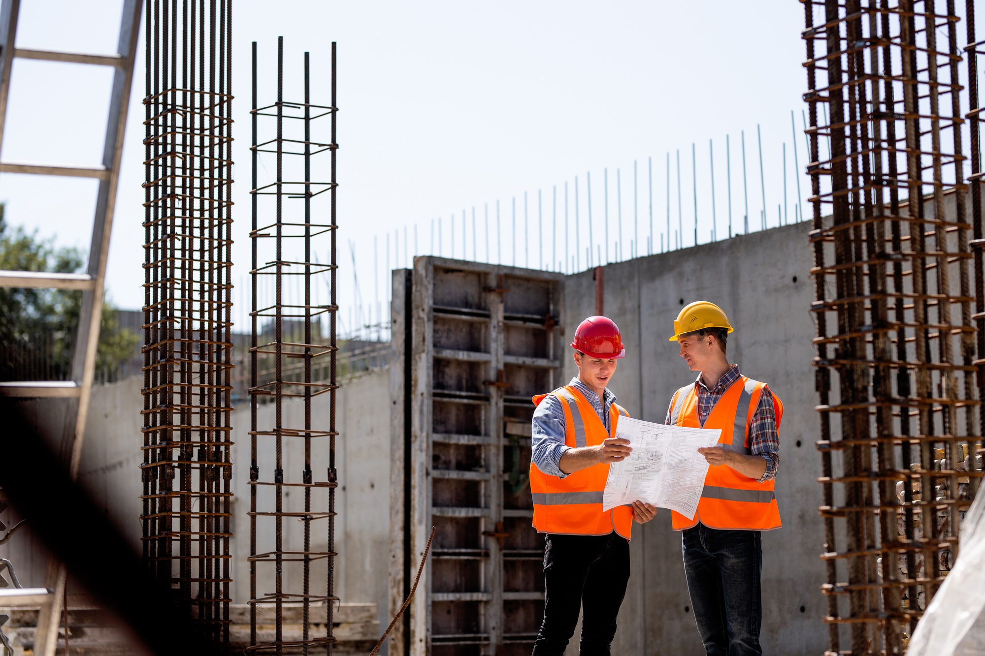 Civil engineer and construction manager in orange work vests and hard helmets explore construction